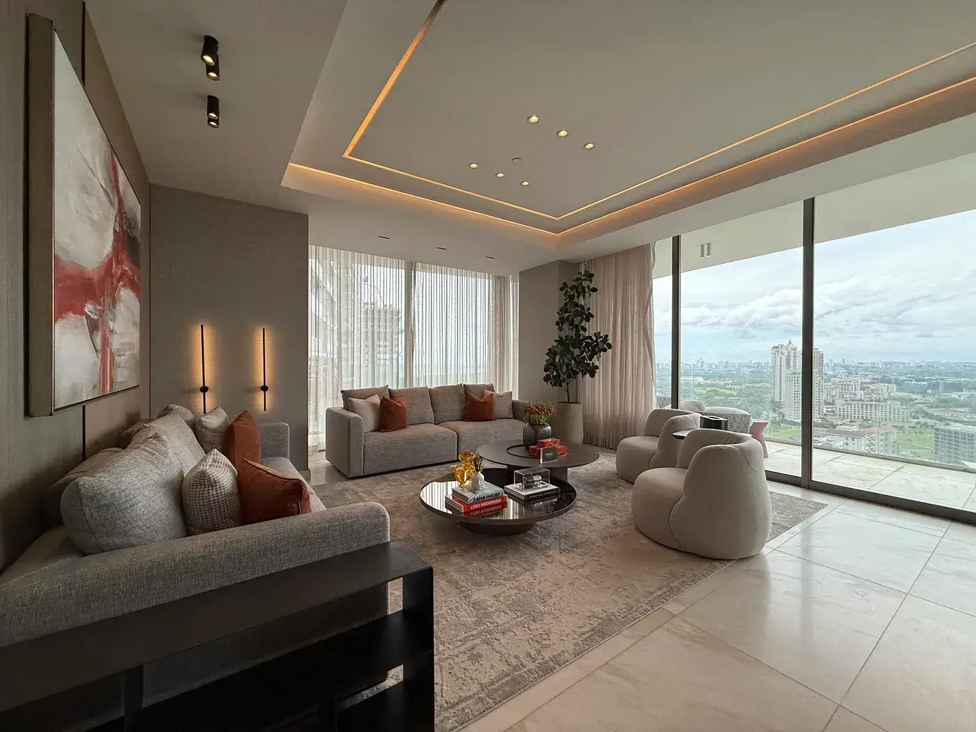 The living room of model apartment 24D at La Maison, with a cove-lit tray ceiling, deep sofas and floor-to-ceiling glazing over Santa María and the city beyond