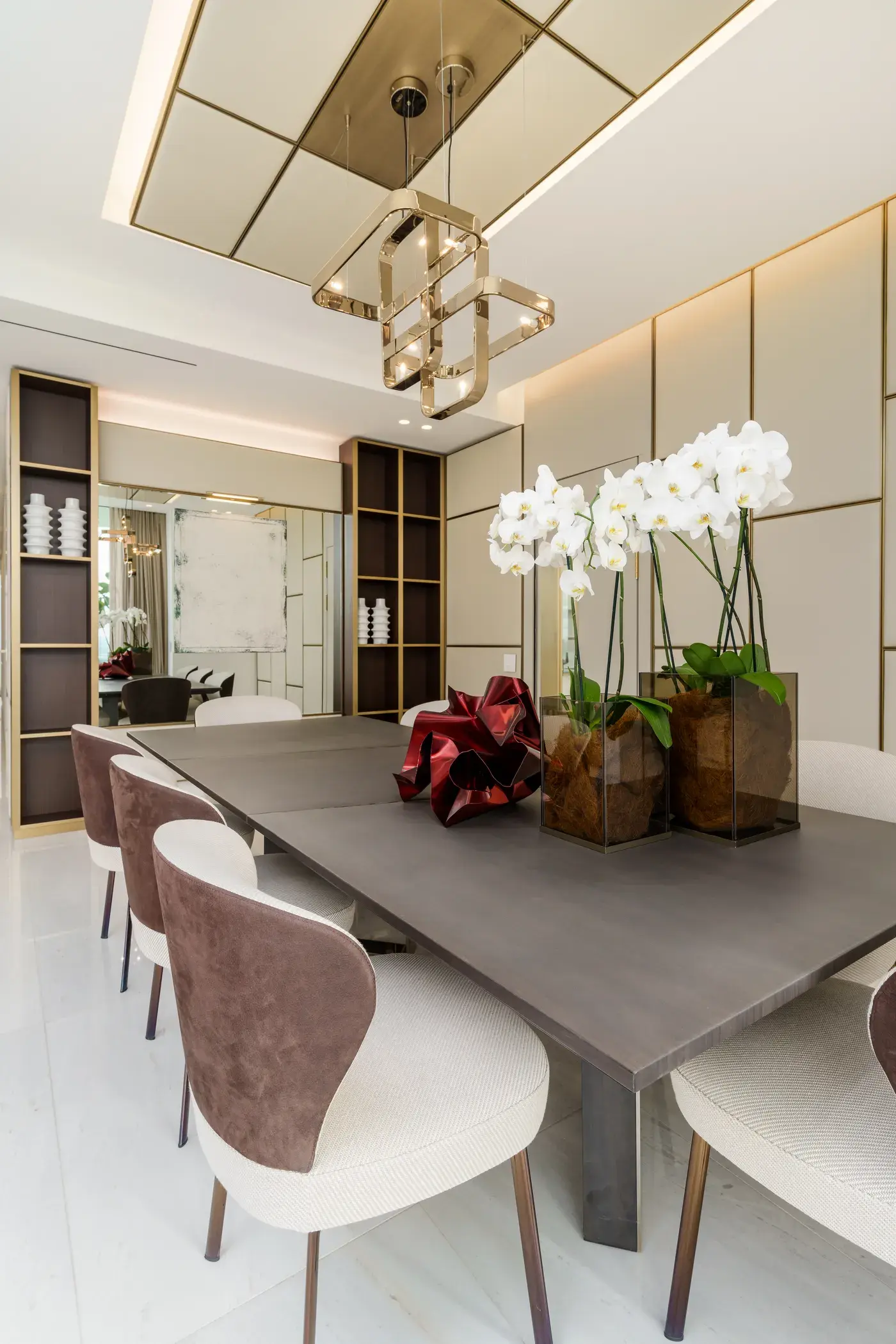 The dining room of the Fendi model apartment, with a sculptural brass chandelier over a stone table, suede and bouclé chairs and white orchids