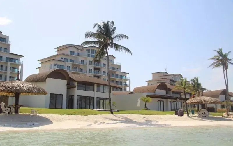 Resort buildings at Playa Escondida behind a palm and a thatched pavilion on the sand