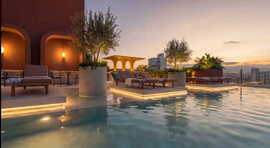 Selvática's rooftop pool at dusk, with lit stone terraces, olive trees in planters and the Panama City skyline beyond
