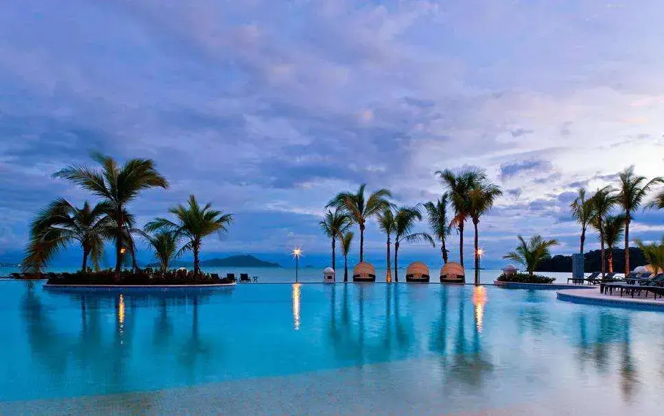 The infinity pool at Playa Bonita at dusk, palms silhouetted against the water and the bay